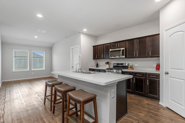 kitchen with stainless steel appliances, an island with sink, sink, dark hardwood / wood-style floors, and a breakfast bar area