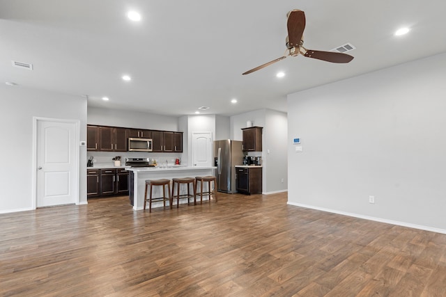 kitchen with hardwood / wood-style flooring, an island with sink, a breakfast bar area, stainless steel appliances, and ceiling fan