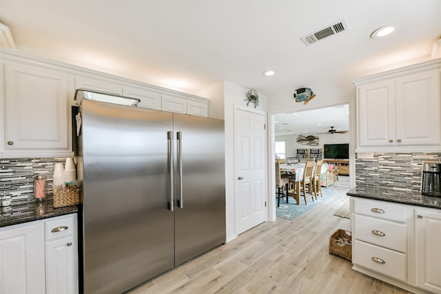 kitchen featuring decorative backsplash, dark stone countertops, built in fridge, and white cabinetry