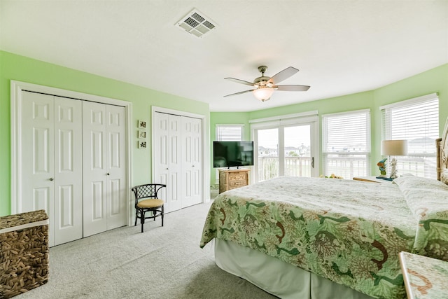 bedroom with ceiling fan, two closets, multiple windows, and light carpet