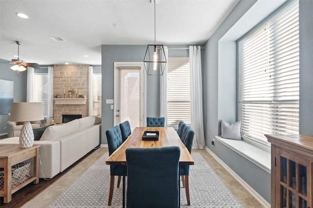 dining room with ceiling fan, a healthy amount of sunlight, a fireplace, and light tile patterned floors