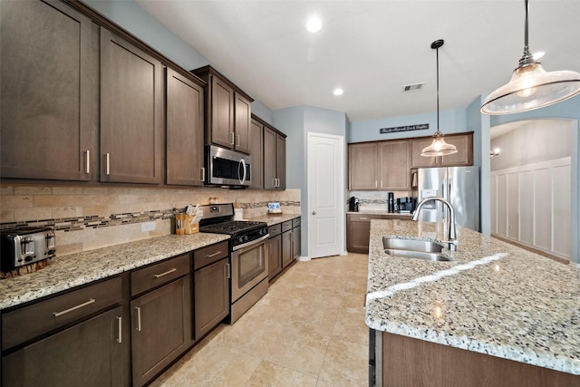 kitchen with sink, hanging light fixtures, a kitchen island with sink, stainless steel appliances, and dark brown cabinets