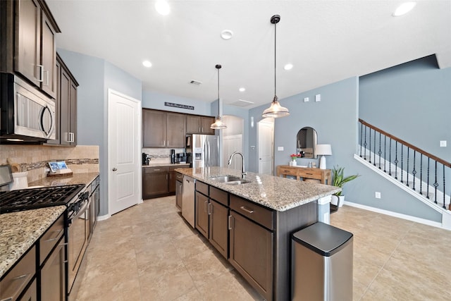 kitchen with light stone countertops, stainless steel appliances, sink, a kitchen island with sink, and dark brown cabinets