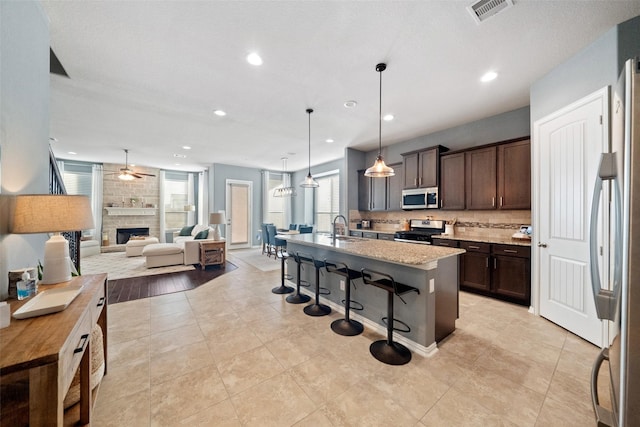 kitchen featuring a center island with sink, sink, hanging light fixtures, a kitchen breakfast bar, and stainless steel appliances