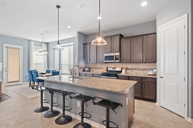 kitchen with appliances with stainless steel finishes, decorative light fixtures, sink, light stone counters, and a center island with sink