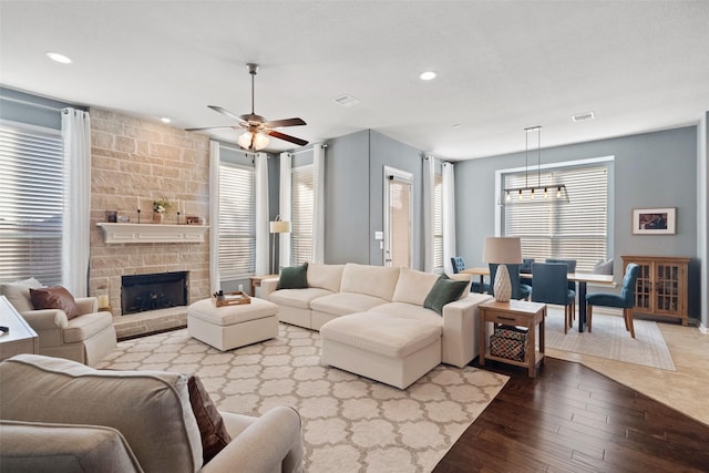 living room featuring a fireplace, a wealth of natural light, ceiling fan with notable chandelier, and hardwood / wood-style flooring