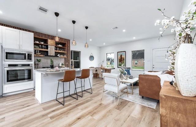 kitchen featuring decorative light fixtures, backsplash, an island with sink, stainless steel appliances, and white cabinets