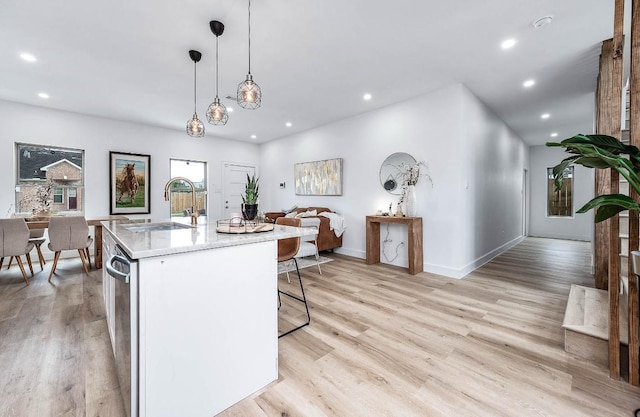 kitchen featuring light hardwood / wood-style floors, a center island with sink, decorative light fixtures, dishwasher, and sink