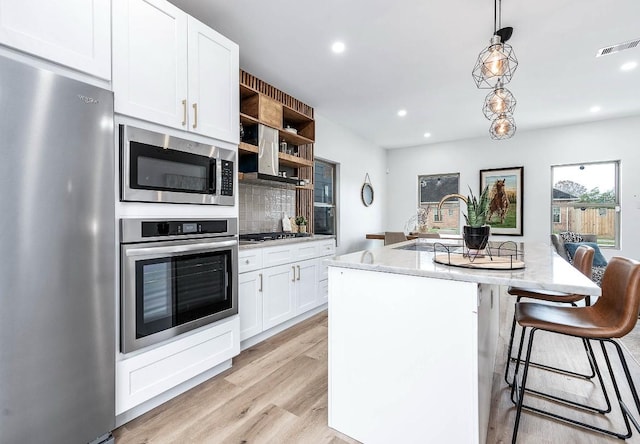 kitchen with tasteful backsplash, hanging light fixtures, a kitchen island with sink, appliances with stainless steel finishes, and white cabinets