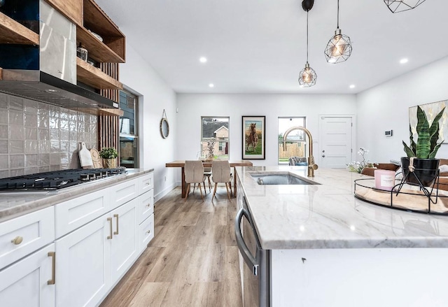 kitchen with pendant lighting, appliances with stainless steel finishes, exhaust hood, white cabinetry, and sink