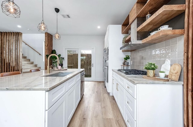 kitchen with white cabinetry, sink, hanging light fixtures, light wood-type flooring, and light stone counters