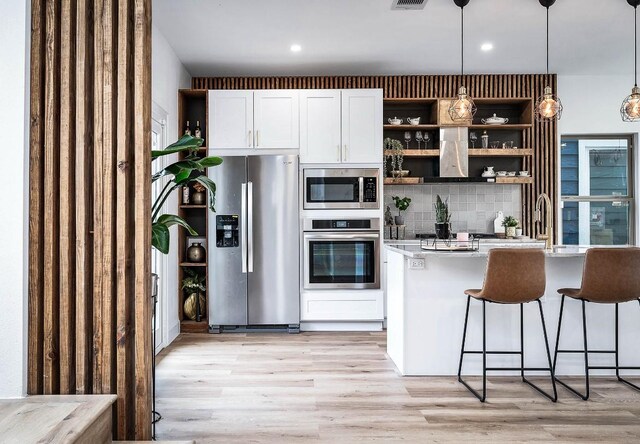 kitchen with pendant lighting, white cabinets, stainless steel appliances, decorative backsplash, and light hardwood / wood-style flooring