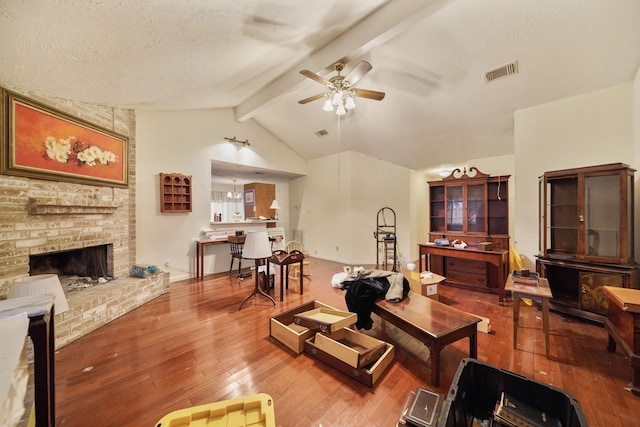 living room with ceiling fan with notable chandelier, a textured ceiling, hardwood / wood-style floors, lofted ceiling with beams, and a brick fireplace