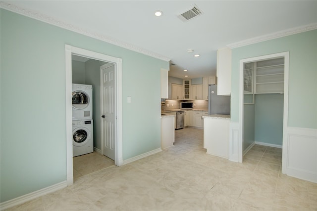 kitchen with white cabinets, appliances with stainless steel finishes, stacked washer and clothes dryer, light stone counters, and crown molding