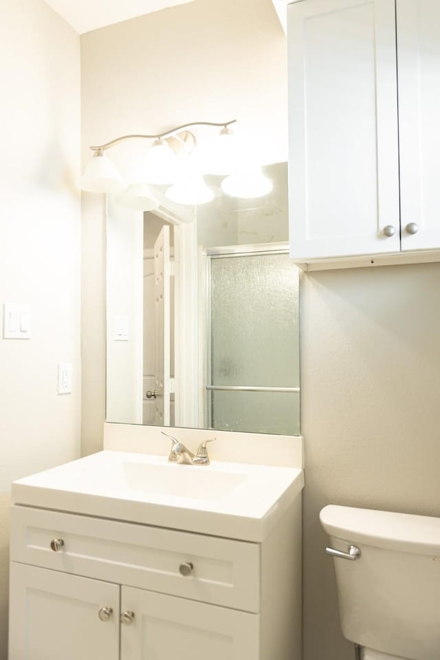 bathroom featuring toilet, vanity, and a shower with shower door