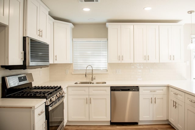 kitchen with white cabinetry, appliances with stainless steel finishes, decorative backsplash, hanging light fixtures, and sink