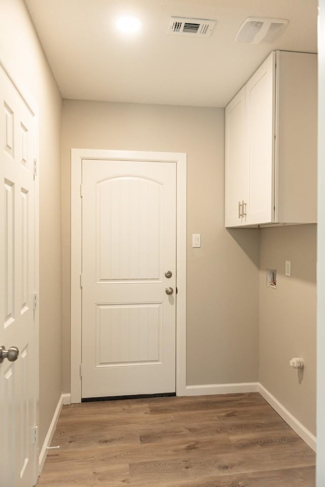 washroom with hookup for a washing machine, light hardwood / wood-style floors, and cabinets