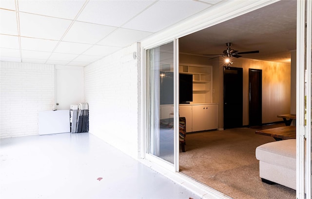 interior space with ceiling fan, a drop ceiling, and brick wall