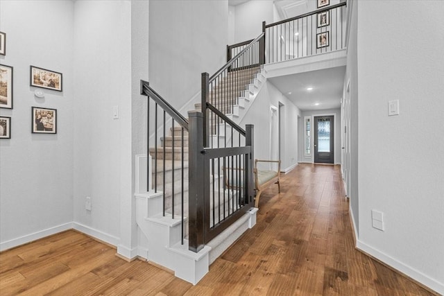 stairway featuring baseboards, wood finished floors, and a towering ceiling