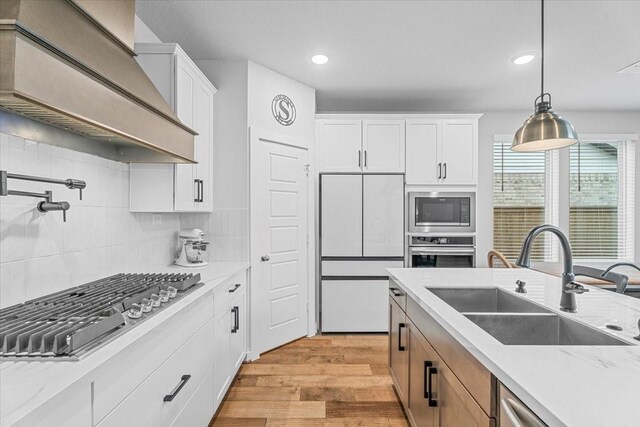 kitchen with custom exhaust hood, light stone countertops, appliances with stainless steel finishes, white cabinetry, and sink