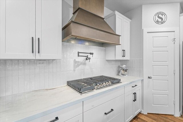 kitchen with light stone countertops, custom exhaust hood, white cabinetry, decorative backsplash, and stainless steel gas cooktop