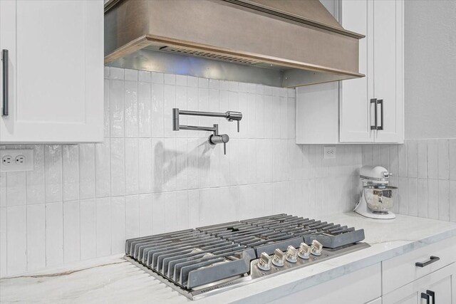 interior details featuring light stone counters, white cabinetry, stainless steel gas stovetop, and custom range hood