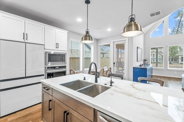 kitchen with hanging light fixtures, sink, white cabinetry, light stone countertops, and stainless steel appliances