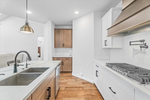 kitchen with appliances with stainless steel finishes, custom exhaust hood, decorative light fixtures, white cabinetry, and sink