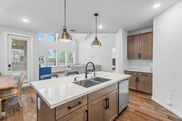 kitchen with dishwasher, sink, decorative light fixtures, backsplash, and a center island with sink