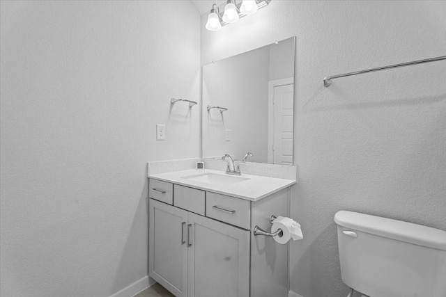 half bathroom with baseboards, toilet, vanity, and a textured wall