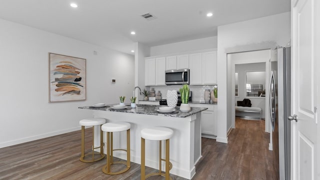 kitchen with white cabinets, stainless steel appliances, dark stone counters, and a kitchen island with sink