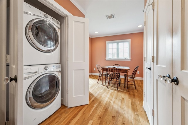 washroom featuring stacked washing maching and dryer, crown molding, and light hardwood / wood-style flooring