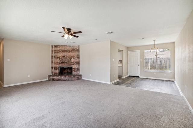 unfurnished living room with ceiling fan with notable chandelier, a fireplace, and dark colored carpet