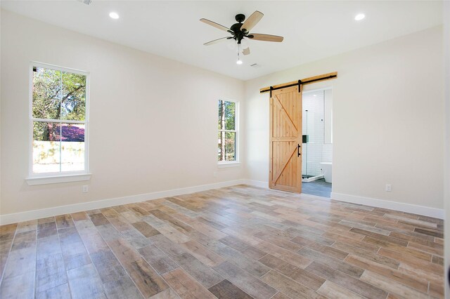 unfurnished bedroom featuring ceiling fan, a barn door, ensuite bathroom, and light hardwood / wood-style floors