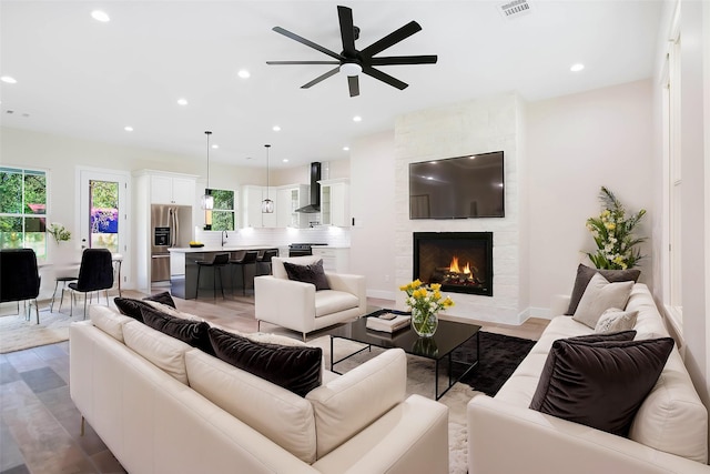 living room with ceiling fan, a large fireplace, and wood-type flooring