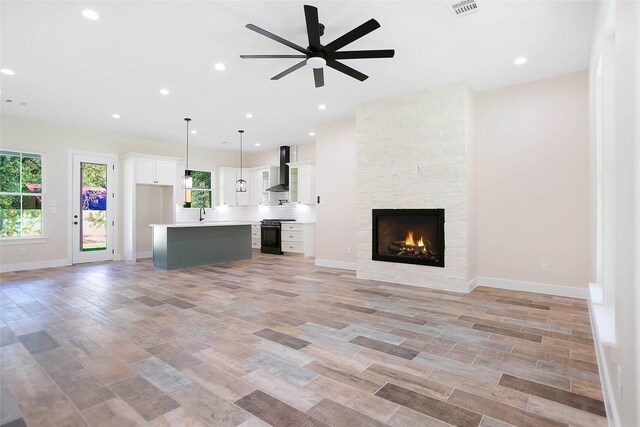 unfurnished living room with ceiling fan, a tiled fireplace, and light hardwood / wood-style flooring