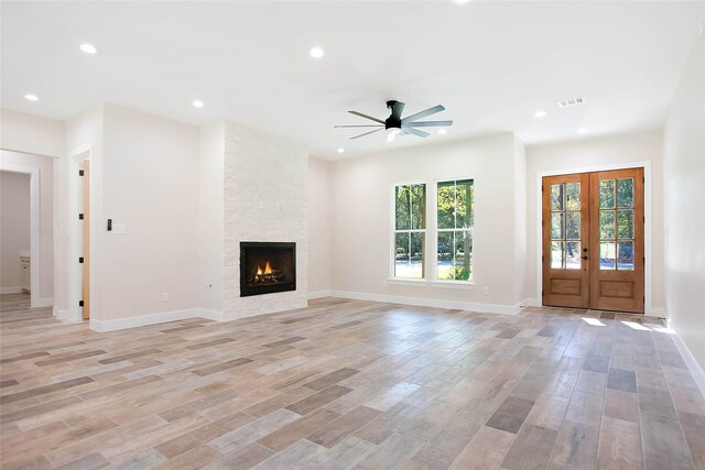 unfurnished living room with ceiling fan, a stone fireplace, french doors, and light wood-type flooring