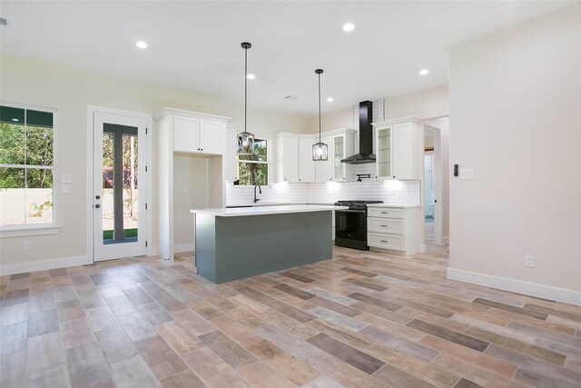 kitchen with black range oven, decorative light fixtures, wall chimney range hood, white cabinets, and a center island