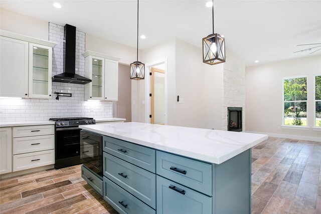 kitchen with black appliances, pendant lighting, wall chimney exhaust hood, white cabinets, and a center island