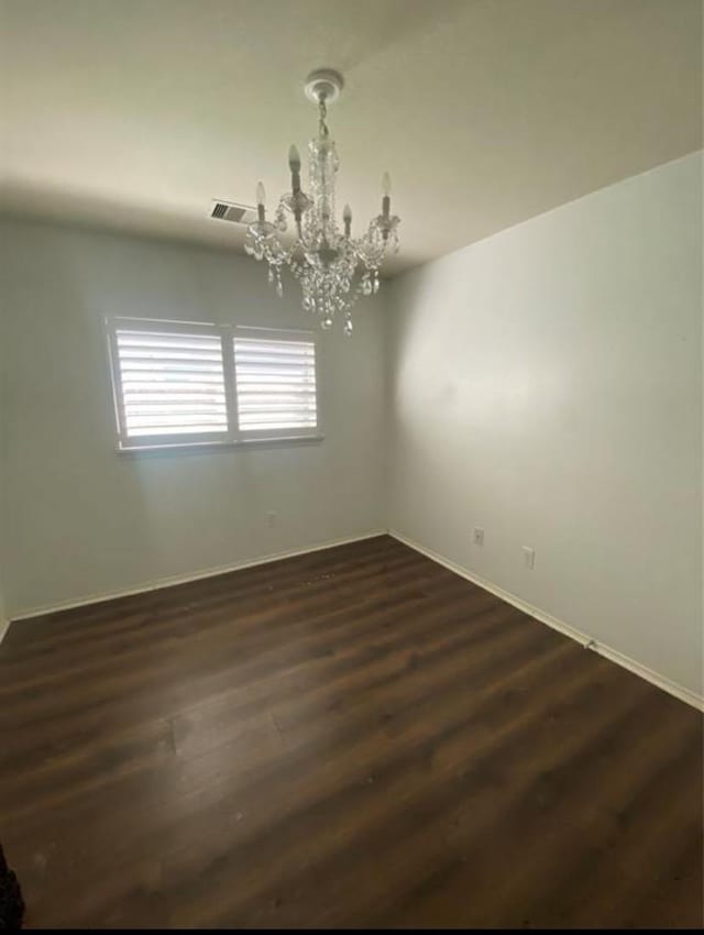 spare room with dark hardwood / wood-style flooring and a chandelier