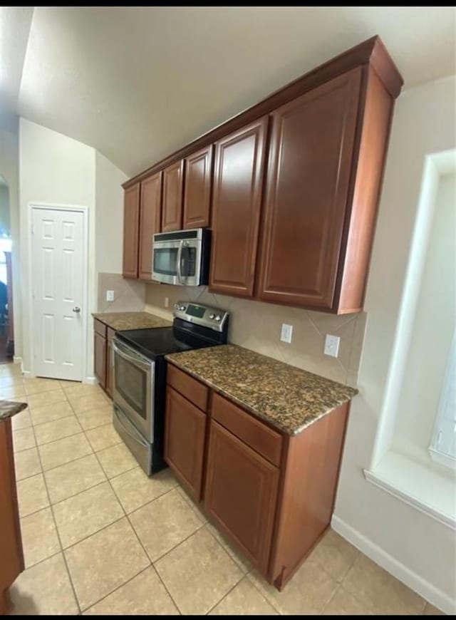 kitchen featuring vaulted ceiling, light tile patterned floors, stainless steel appliances, and dark stone countertops