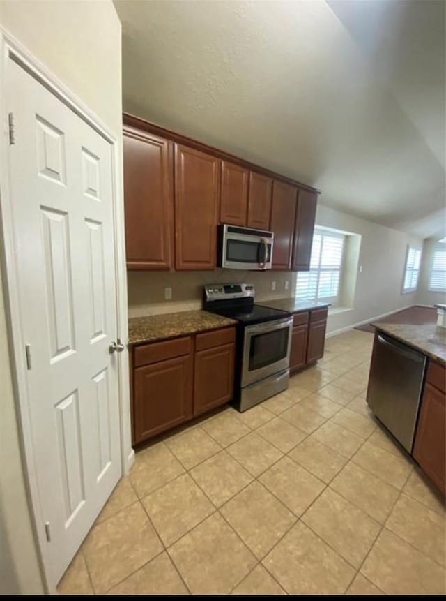 kitchen with appliances with stainless steel finishes, dark stone counters, and light tile patterned flooring