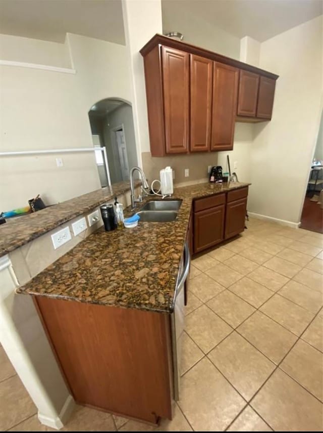 kitchen featuring light tile patterned flooring, kitchen peninsula, dark stone counters, and sink