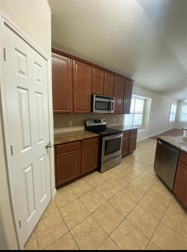 kitchen with light tile patterned floors, dark stone countertops, and stainless steel appliances