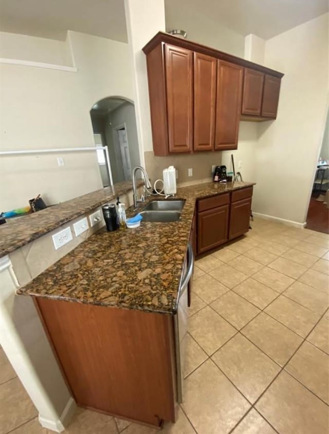 kitchen with sink, light tile patterned floors, kitchen peninsula, and dark stone countertops