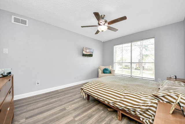 bedroom with a textured ceiling, ceiling fan, and dark hardwood / wood-style flooring