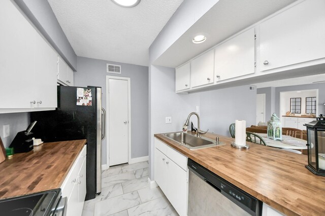 kitchen with white cabinetry, butcher block countertops, stainless steel appliances, a textured ceiling, and sink