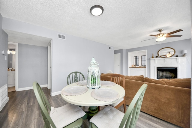 dining area with ceiling fan, a brick fireplace, a textured ceiling, and hardwood / wood-style flooring