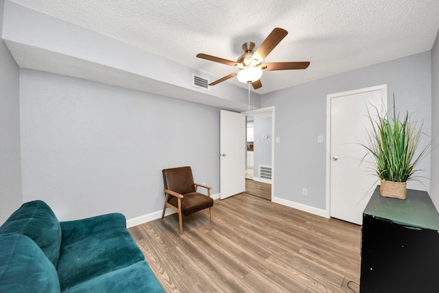 living area with ceiling fan, a textured ceiling, and hardwood / wood-style floors