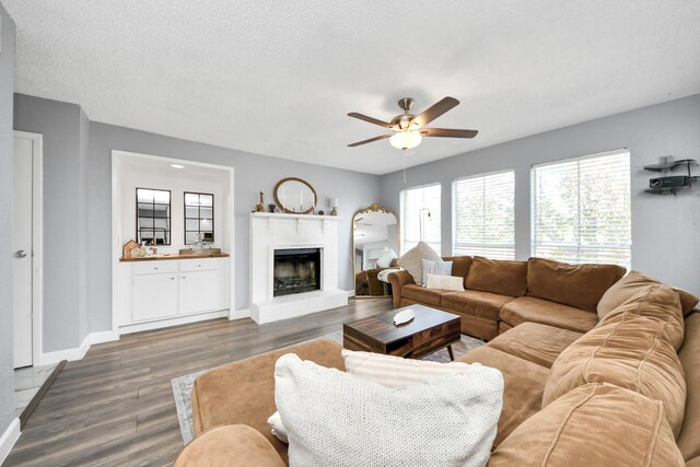 living room with a textured ceiling, dark wood-type flooring, a brick fireplace, and ceiling fan